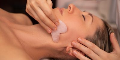 Young and beautiful woman during Chinese traditional massage - Gua Sha with stone. Close-up photo. Beauty treatment in SPA salon. Anti-aging skin care